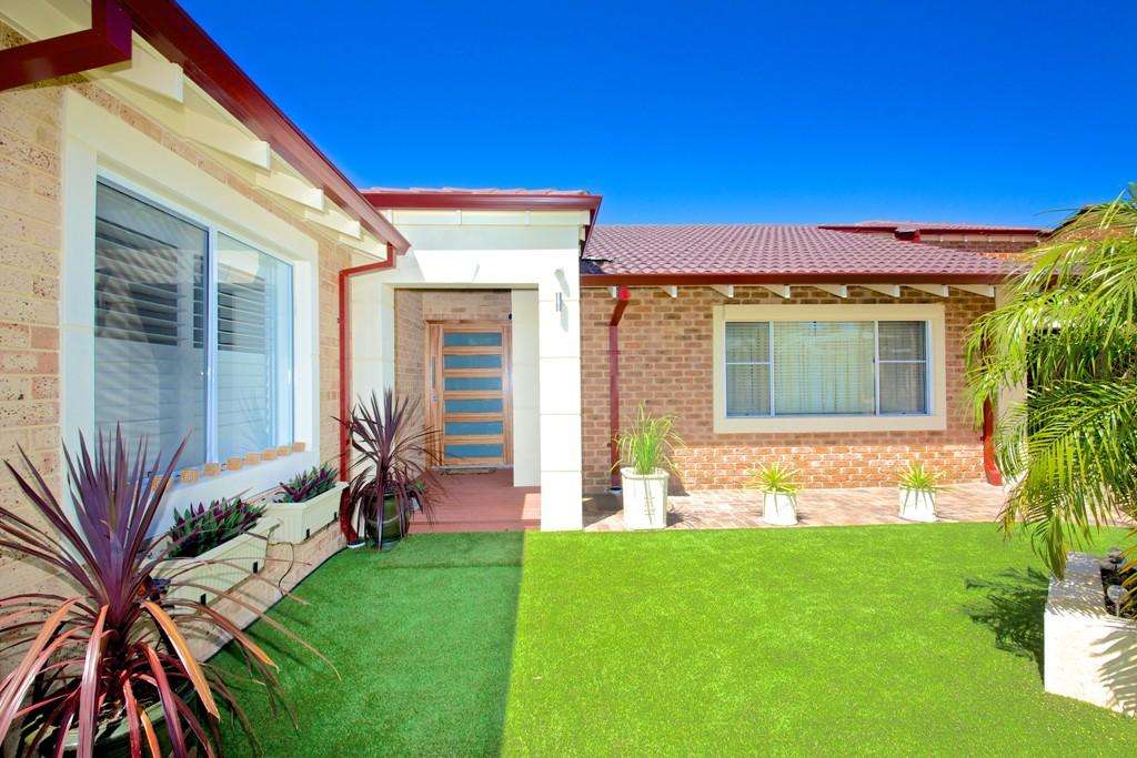 A modern Connolly house exterior with brick walls, a frosted glass door, three windows, and a green lawn adorned with potted plants under a clear blue sky offers the perfect blend of style and comfort.