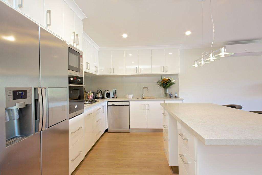Modern kitchen with white cabinets, stainless steel appliances, and a large island. A bouquet of flowers sits on the counter next to small appliances. Ceiling lights hang above the island, adding a touch of elegance to this Connolly home's spacious granny flat.